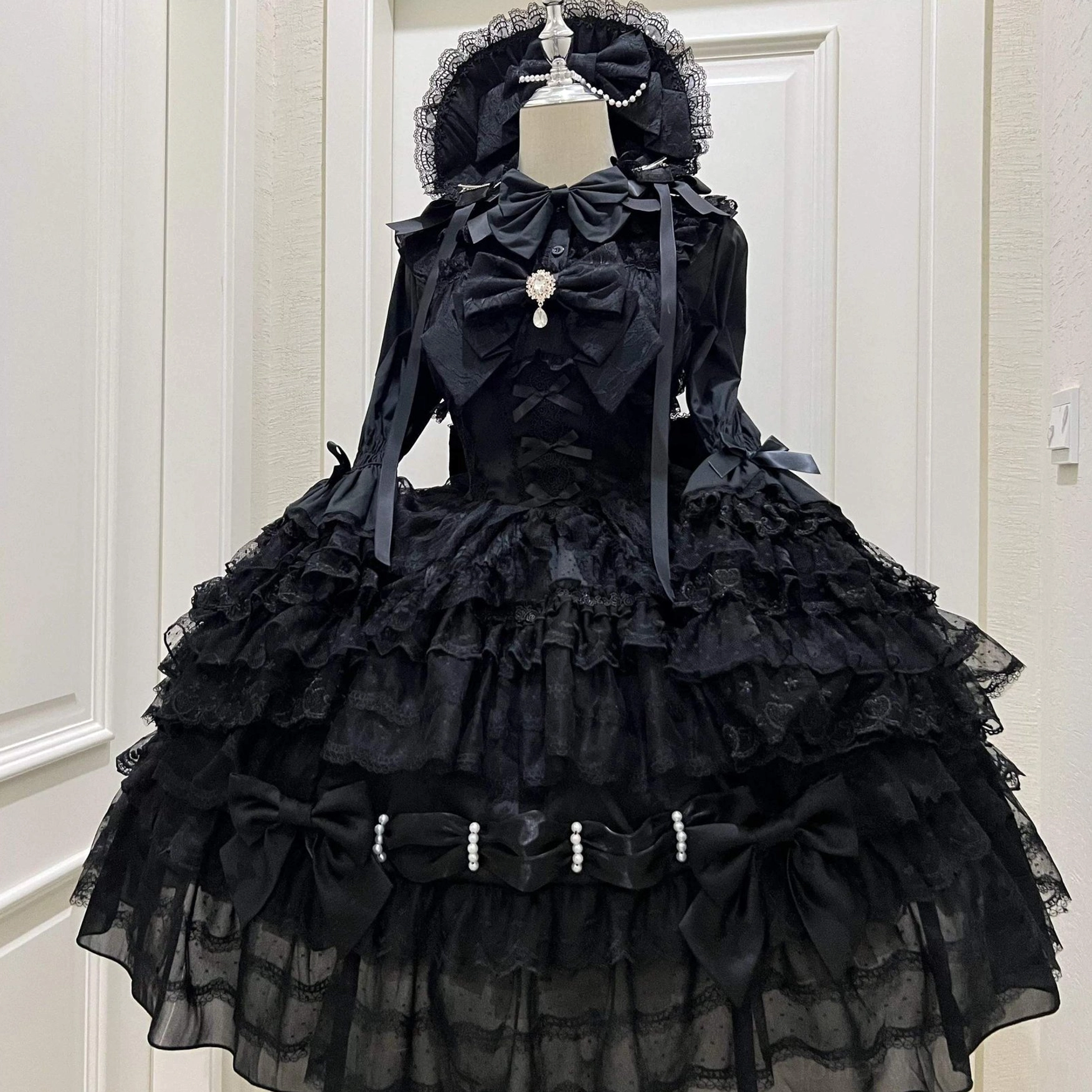 Black Gothic Lolita JSK dress with front bow decorative brooch layered ruffle skirt and pearl-trimmed waist bows front view