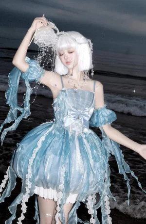 Dreaming Jellyfish sweet lolita JSK dress worn by white-haired model at seaside beach with jellyfish prop, showcasing ice blue bubble skirt and tulle tentacle trims
