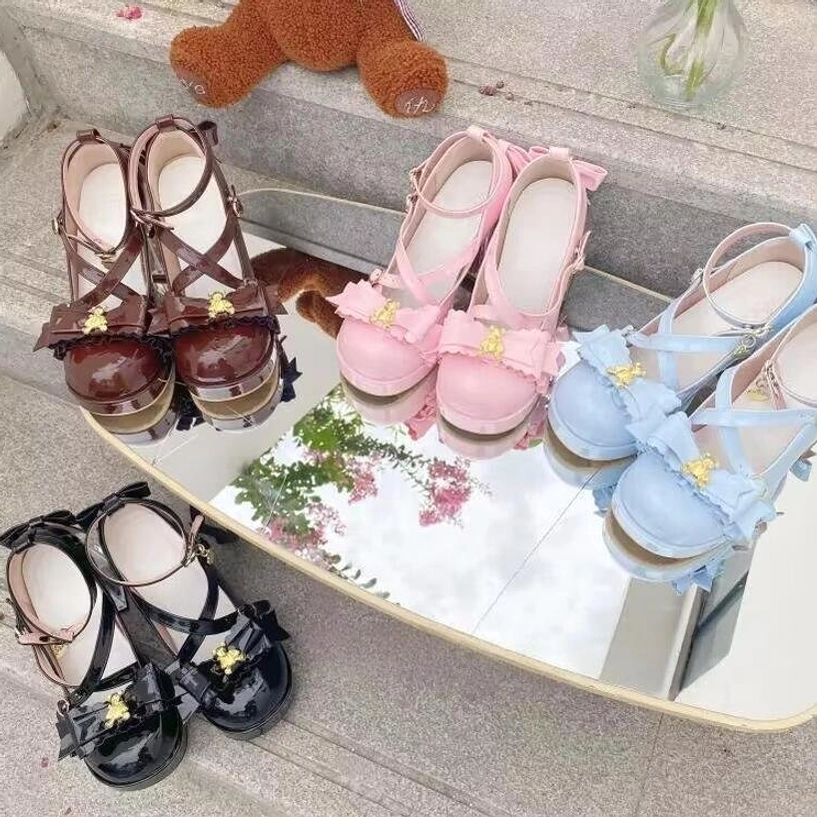 Four pairs of dreamy bear sweet lolita shoes in multiple colorways - light blue, black, pink, white - displayed on staircase with small teddy bear prop, flat lay top-down shot, all featuring cross ankle straps, gold bear charm, clear block heel, round platform toe