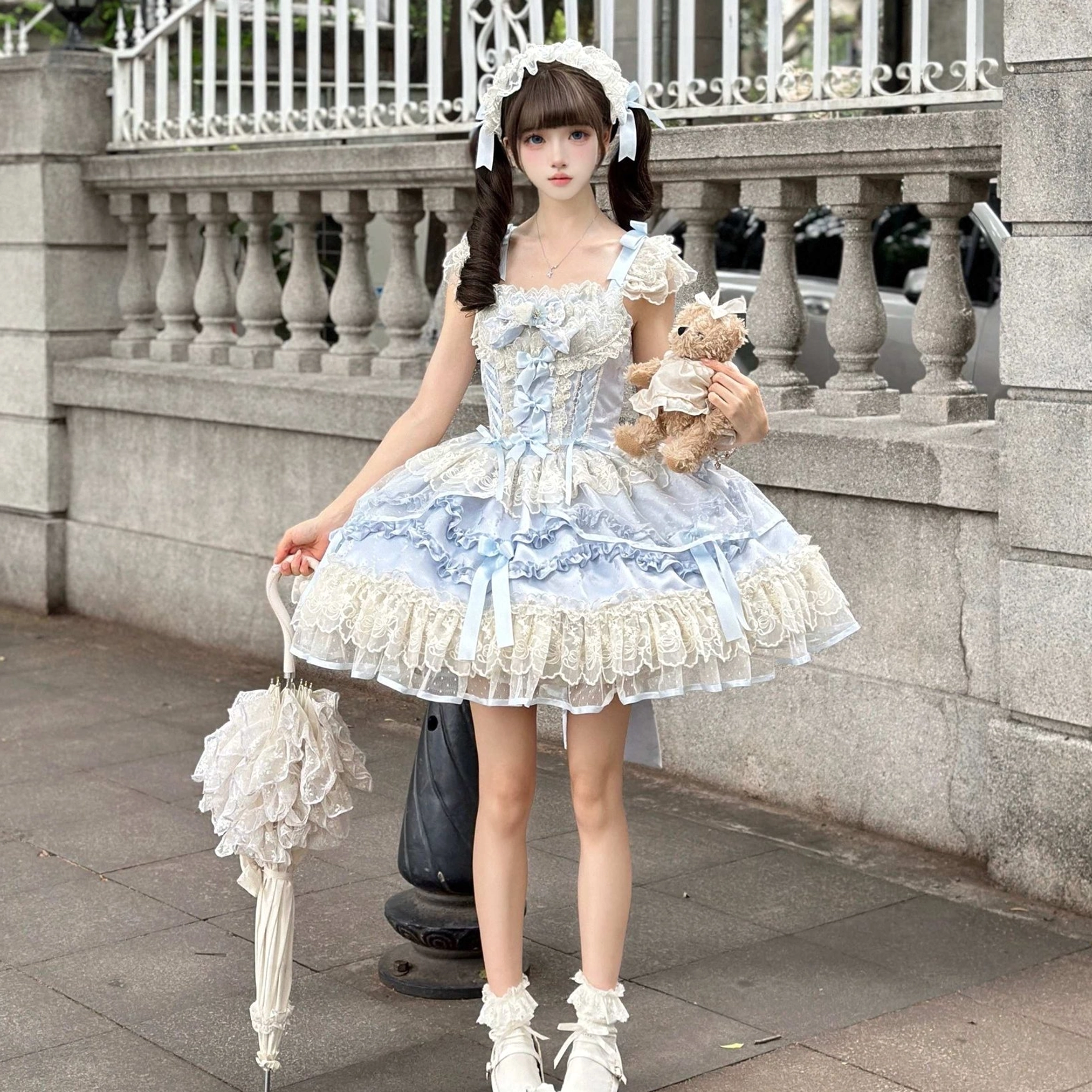 Blue Dreamy Butterfly JSK front eye-level shot outdoor vintage iron balcony, flared lace-trimmed skirt, matching hair headdress, carrying plush teddy bear and folded lace parasol