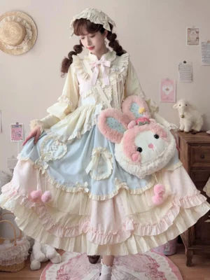 Sweet lolita JSK dress full-body front view in cream and baby blue with pink pom-pom hem details and matching blouse, styled with rabbit crossbody bag in pastel bedroom