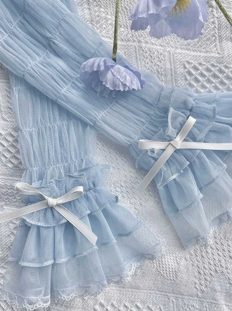 Dusty blue sheer mesh Gothic Lolita arm cuffs with tiered ruffles, satin ribbon bows, and cross design details on white knitted textured background