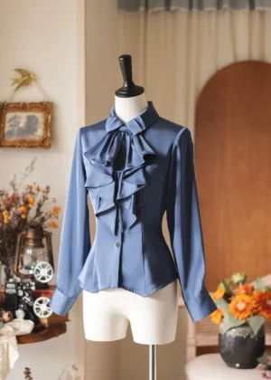 Elegant dusty blue slim-fit Lolita blouse with detachable ruffled jabot collar displayed on dress form, vintage studio setting with floral props