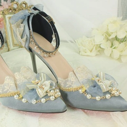 Dusty blue pointed toe Lolita bridal heels overhead flat lay on table with vintage mirror and hydrangea flowers, featuring dusty blue satin upper, light blue bow with pearl decoration, delicate lace trims, pearl ankle strap