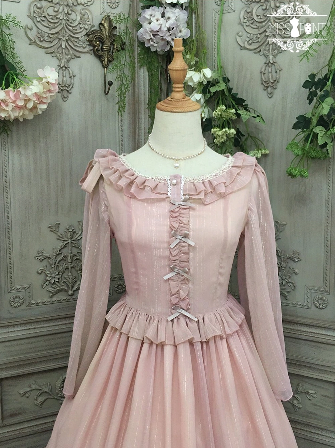 Dusty pink lolita one-piece dress featuring ruffled crew neckline, ruffled waist trim, and full pleated midi skirt with dimensional hem ruffles in sheer striped chiffon fabric, displayed on dress form against ornate vintage background