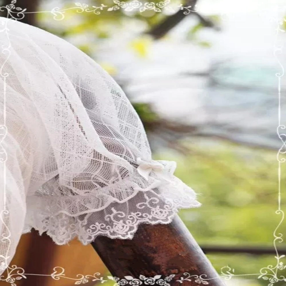 Low-angle side close-up of delicate embroidered lace trim sleeve cuff with small decorative bow detail, blurred water and green foliage backdrop showcasing craftsmanship