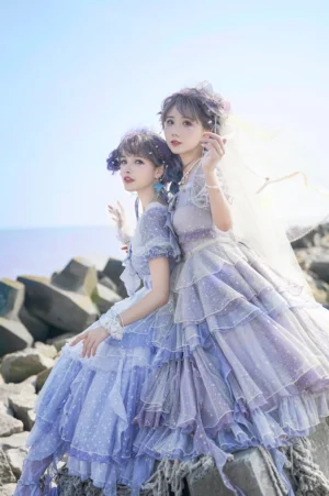 Girl from the Deep Sea Lolita OP dress worn by two models seated at seaside rocky shore, featuring gradient blue-purple layered polka-dot tulle skirt and puff sleeves