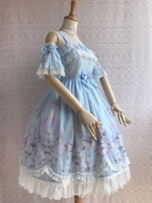 Light blue off-shoulder summer lolita jumper skirt with detachable ruffle sleeves, lace neckline trim, central front bow, scenic garden printed midi skirt, and layered white ruffled bottom shown in three-quarter side view