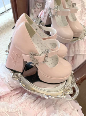 Light pink patent leather Mary Jane platform Lolita heels with silver rose-butterfly buckle and rose-embossed block heel, displayed on vintage mirror and delicate lace fabric