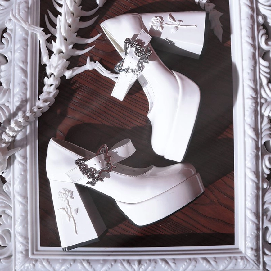 White patent leather Mary Jane platform Lolita heels with silver rose-butterfly buckle and rose-embossed heel, arranged in ornate vintage frame on wooden surface
