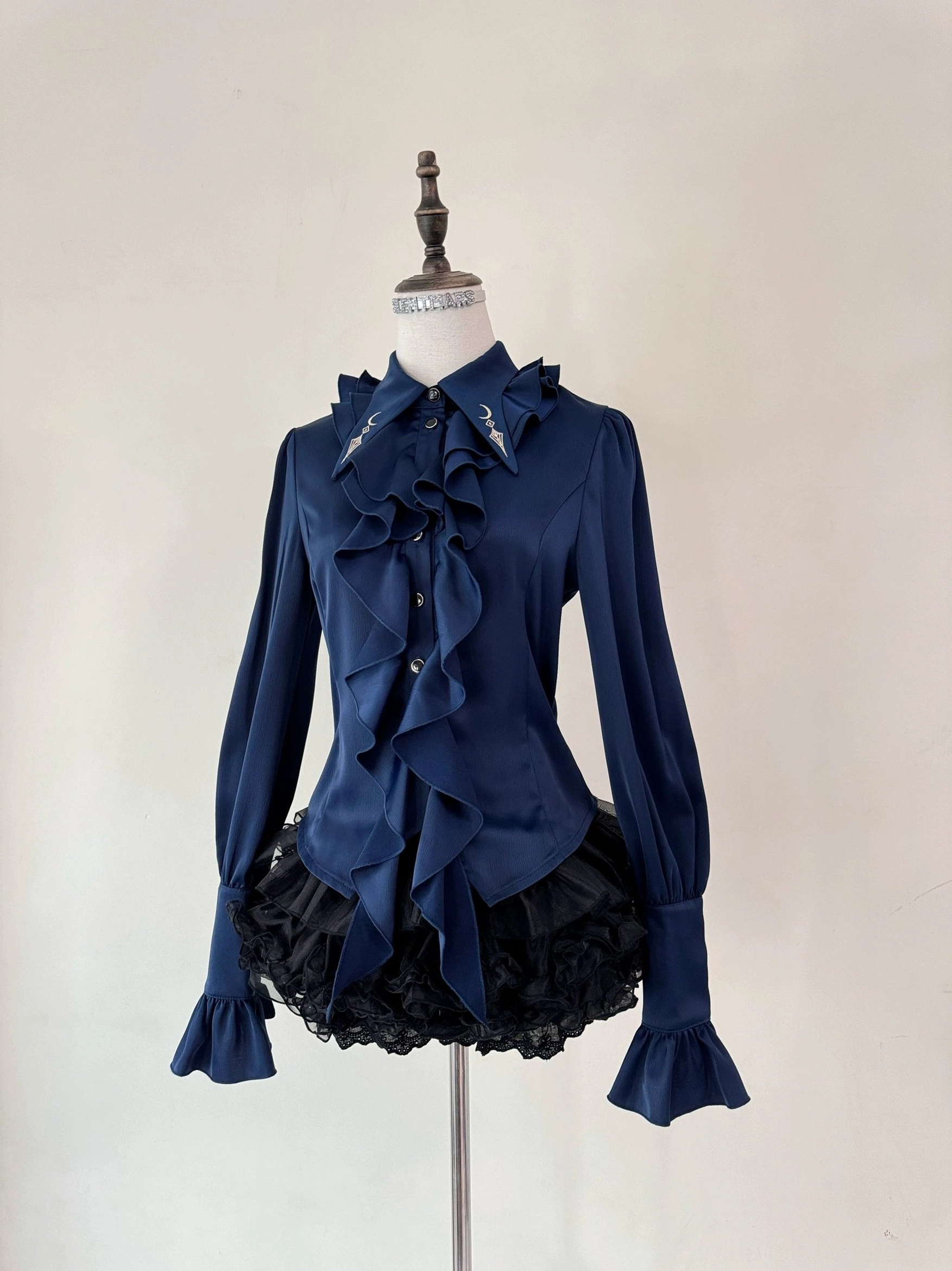 Fallen Moon Rule military lolita blouse and skirt set in navy blue, frontal display on mannequin, featuring stand collar, ruffled front placket, satin fabric sheen, flared long sleeves, and black ruffled underskirt