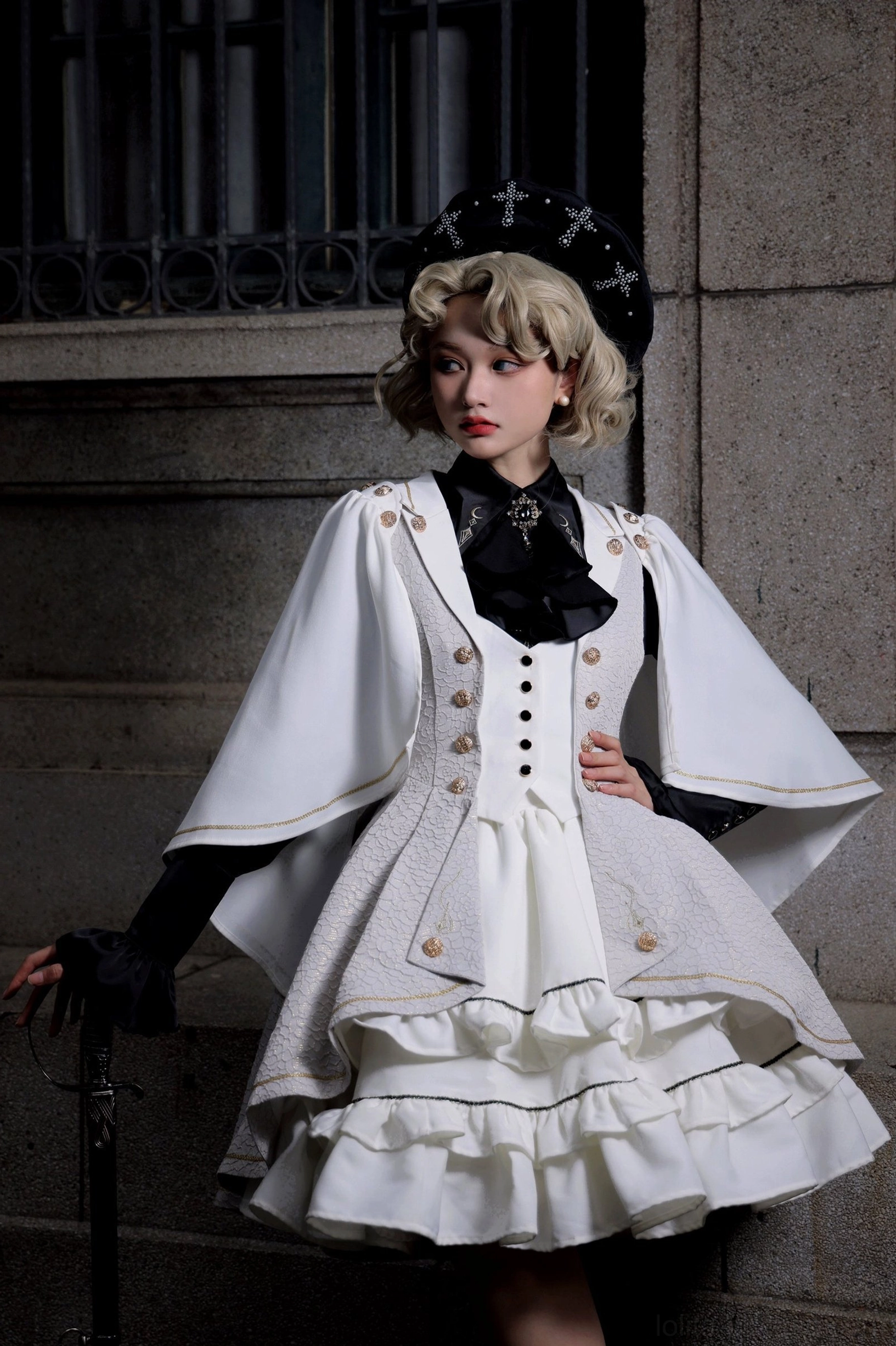 Fallen Moon Rule vintage military lolita dress set in two-tone white and navy, half-body outdoor shot of model wearing vintage hat and black gloves, holding walking cane against stone wall, showcasing tiered ruffled skirt and cape-style sleeves