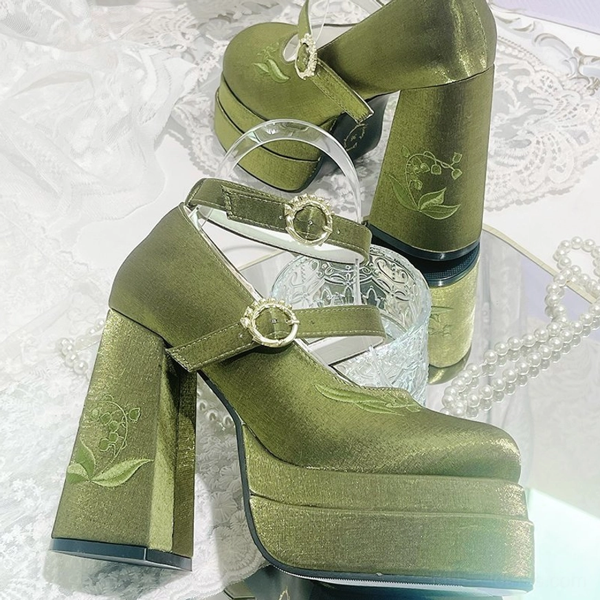 Olive green satin lolita high heel shoes with lily-of-the-valley embroidery, gold buckles, and thick platform heel, flat lay product display on lace tablecloth with pearl ornaments