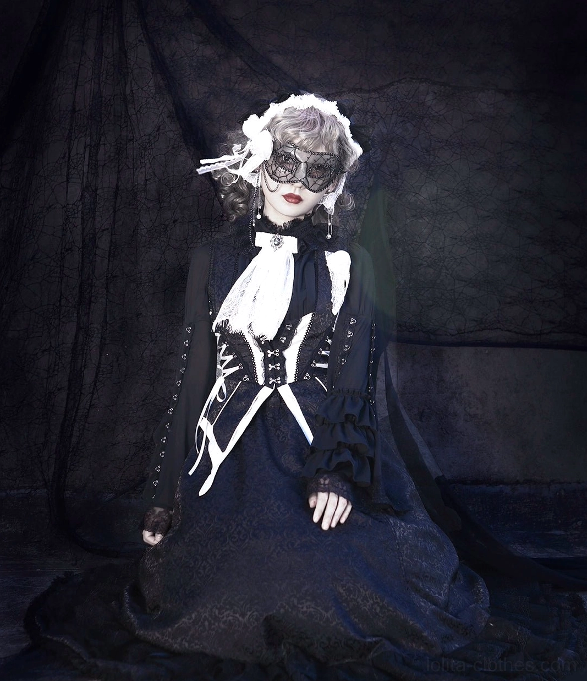 Floor-length gothic lolita dress ensemble seated view displaying white flower hairband, delicate lace sleeve detail, all-black lace floor-length construction, white skeleton corset decoration, and refined elegance