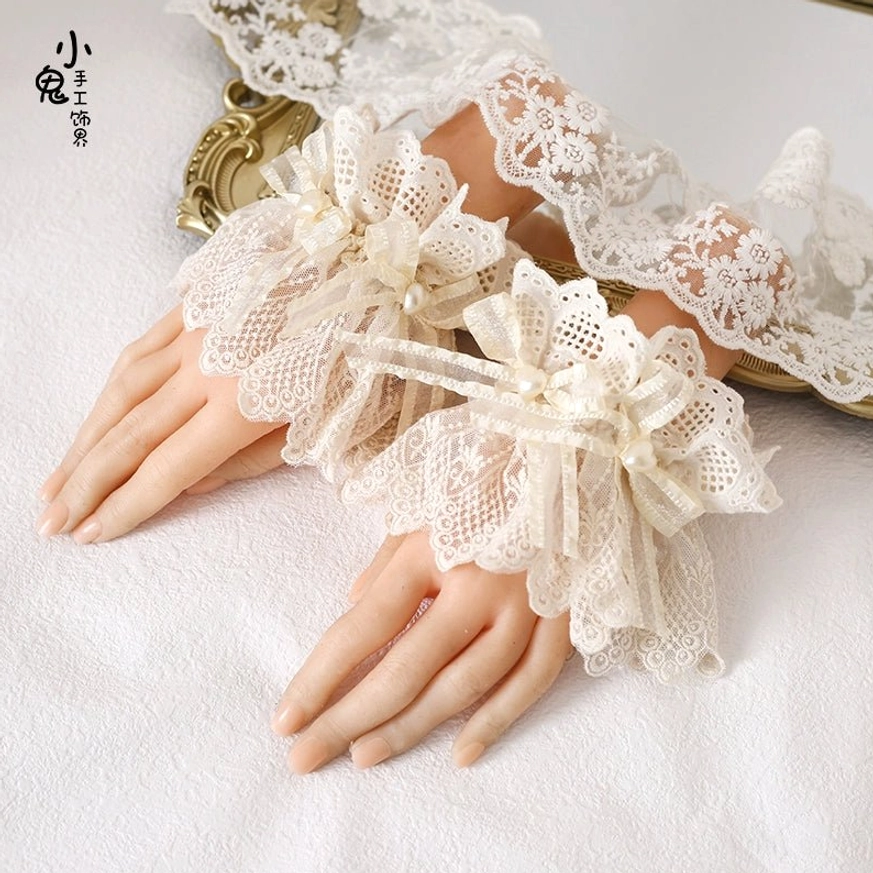 Pair of floral hollow lace wrist cuffs with gathered satin bow details displayed on decorative mannequin hands with gold mirror backdrop