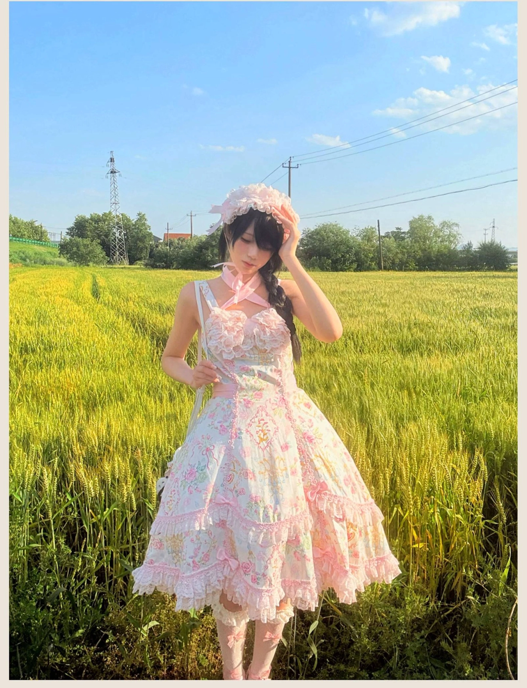 Pink floral Lolita JSK dress with petal hem lace trim and sweetheart neckline shown in side view on model in sunny outdoor wheat field