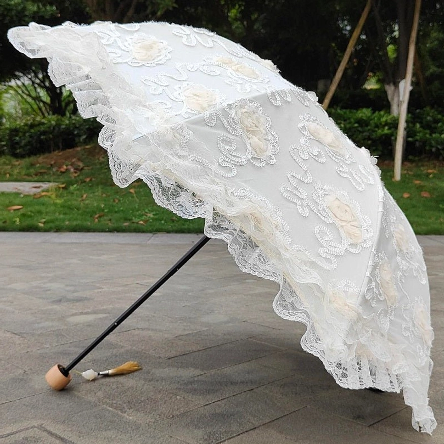 High side view of cream white lolita lace parasol in park setting with green lawn background, featuring wooden handle with decorative tassel pendant and ruffled lace trim along canopy edge