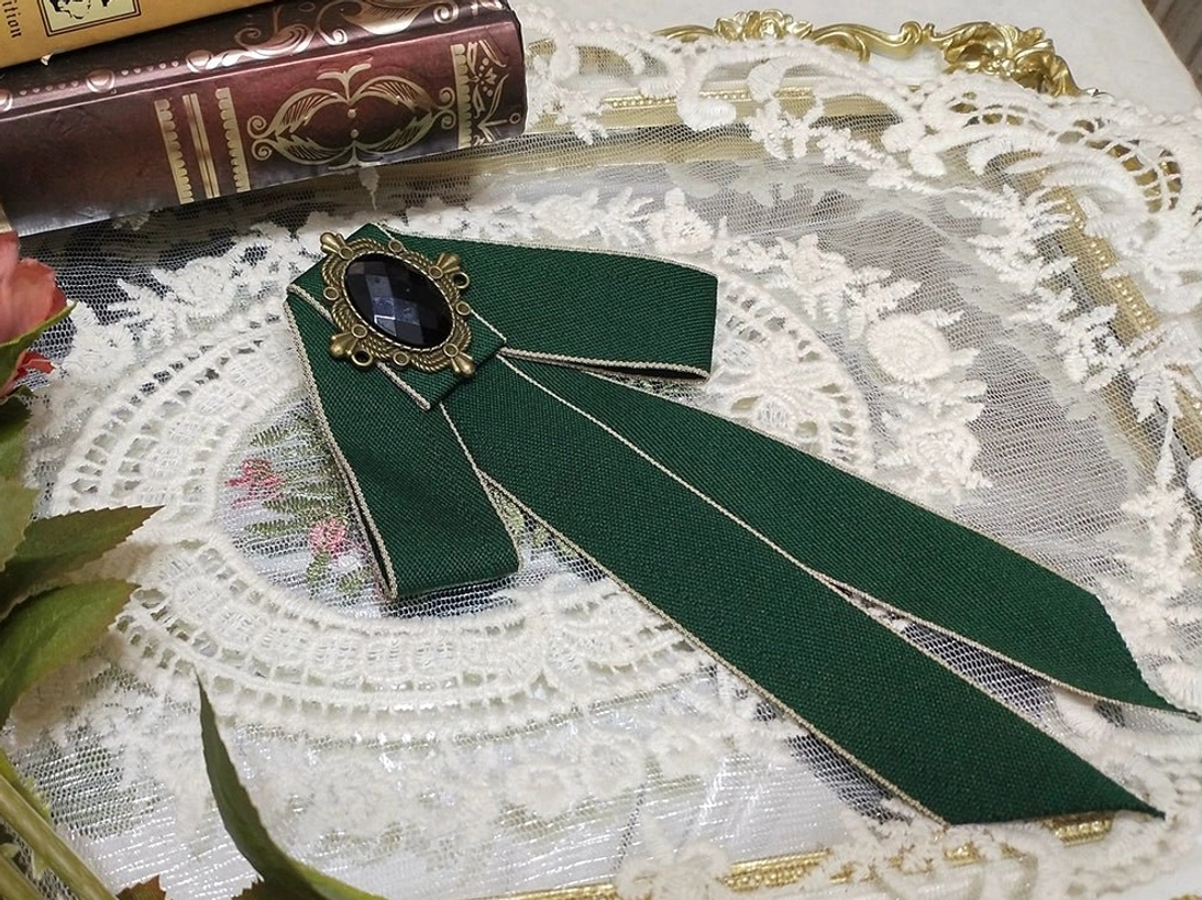 forest-green-lolita-ribbon-bow-brooch-gold-edging-oval-black-gemstone-bronze-metal-frame-white-lace-doily-vintage-books-prop-styling