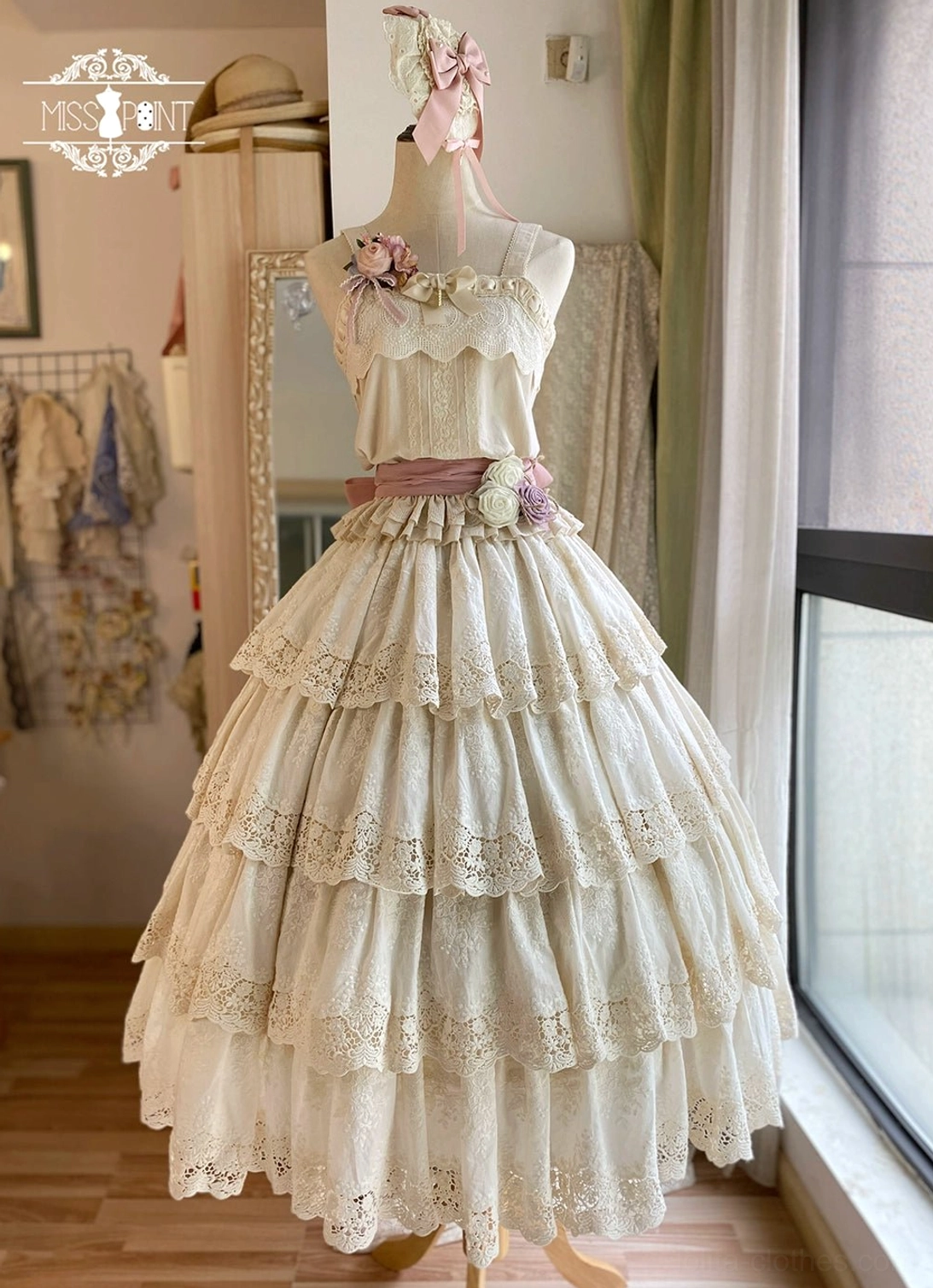Cream beige Forest Waltz lolita camisole with tiered lace skirt pairing, pink waist sash, and floral decorative accents - full length mannequin display with wooden floor backdrop