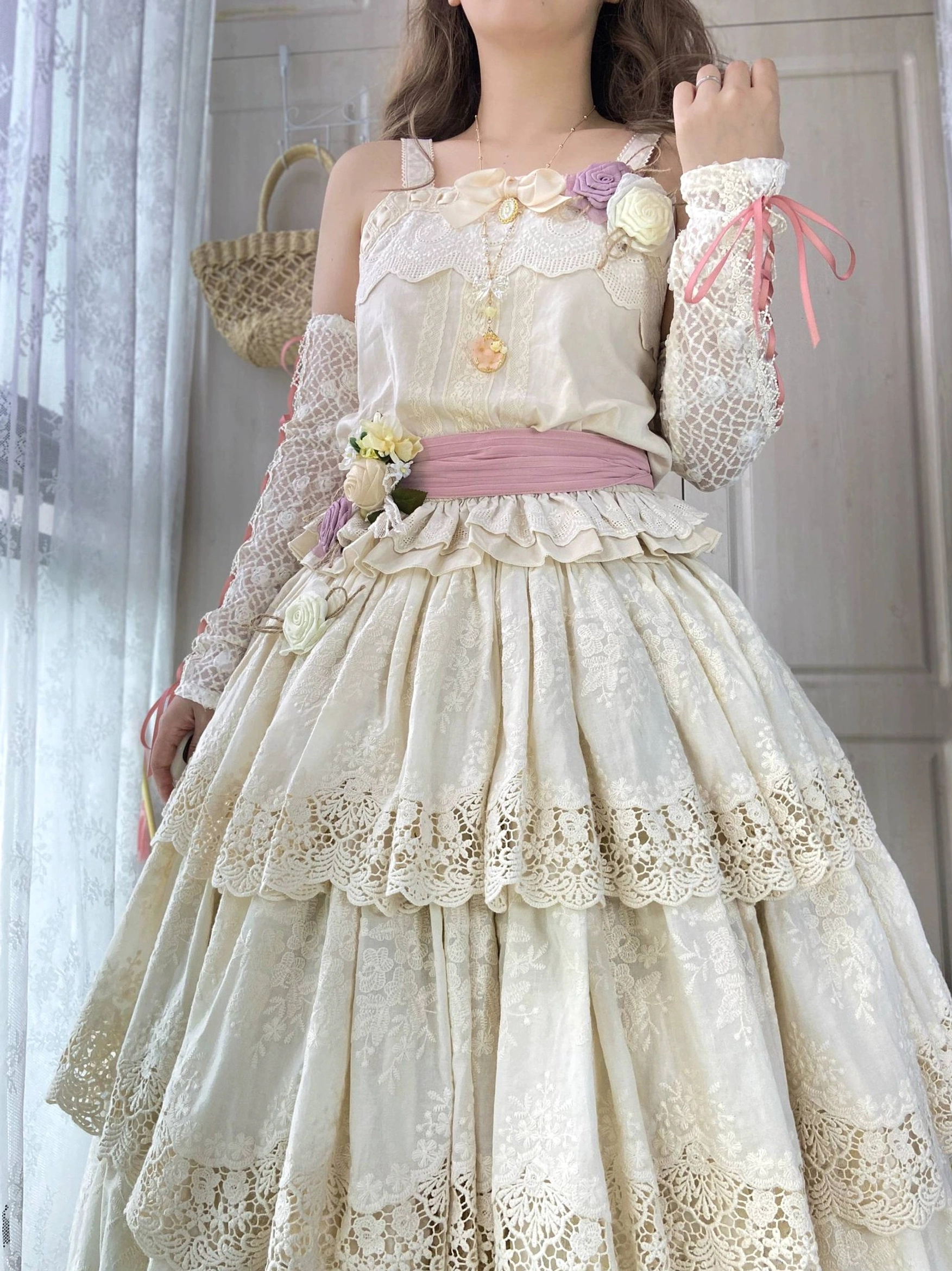 Cream beige Forest Waltz lolita camisole with lace arm sleeves, pink ribbon accents, layered ruffled skirt, floral and sash waist decoration in side partial view on model indoors