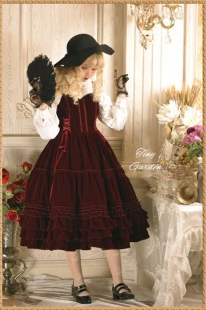 Burgundy velvet Lolita JSK dress full body model wearing square sweetheart neckline with layered ruffle midi skirt white blouse black fedora feather fan vintage indoor scene