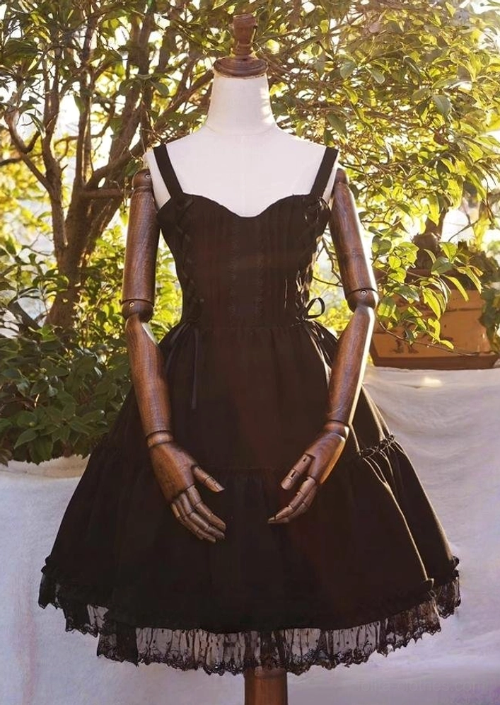 Garden Waltz black lolita JSK dress front full-body mannequin display on wooden jointed stand with green plant background showing sweetheart spaghetti straps lace-up bodice tiered lace hem skirt pure black elegant silhouette