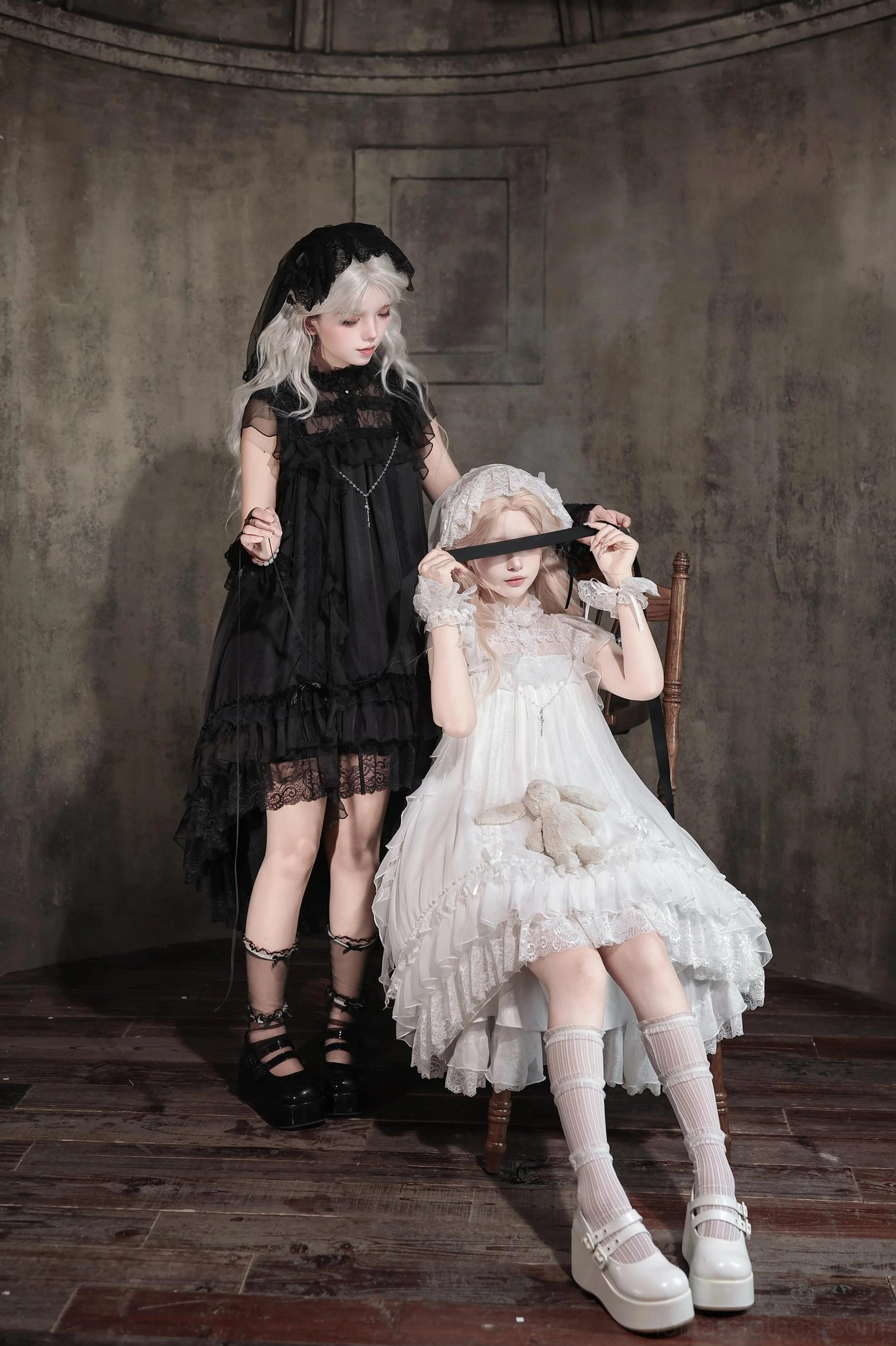 Black and white gothic lolita OP dresses displayed on models in dark vintage room with standing and sitting poses