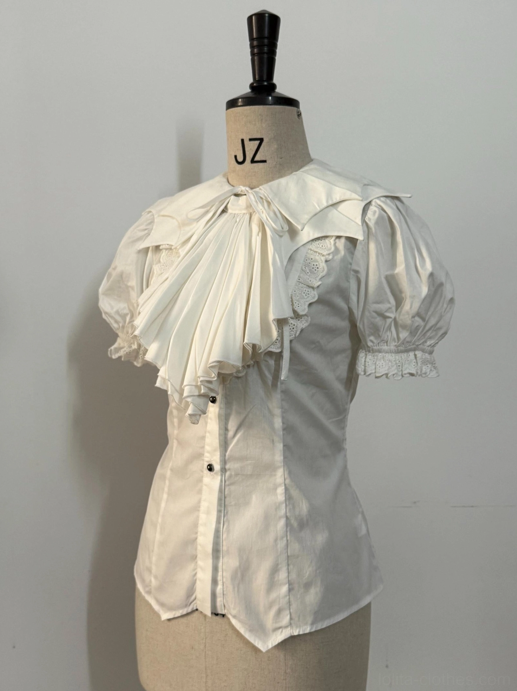 Off-white Gothic Lolita bat-collar shirt with detachable pleated jabot displayed on dress form, featuring puffed short sleeves and fitted waist silhouette