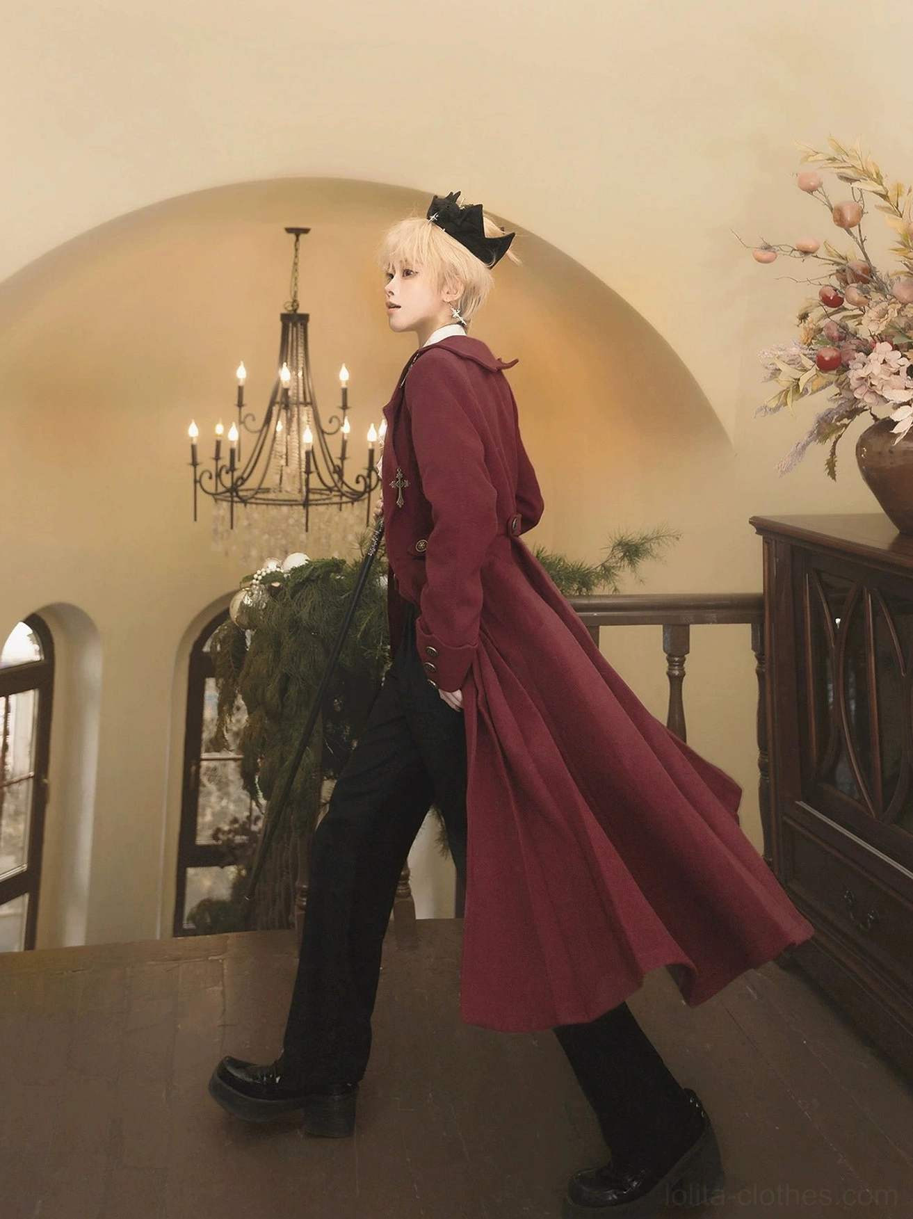 Gothic ouji lolita winter coat back view displaying flowing floor-length burgundy velvet hem black formal shoes vintage wooden balcony european architectural background