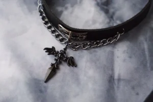 Close-up flat lay of gothic cross leather choker showing detailed embossed metal cross pendant, black leather construction, and metal chain hardware