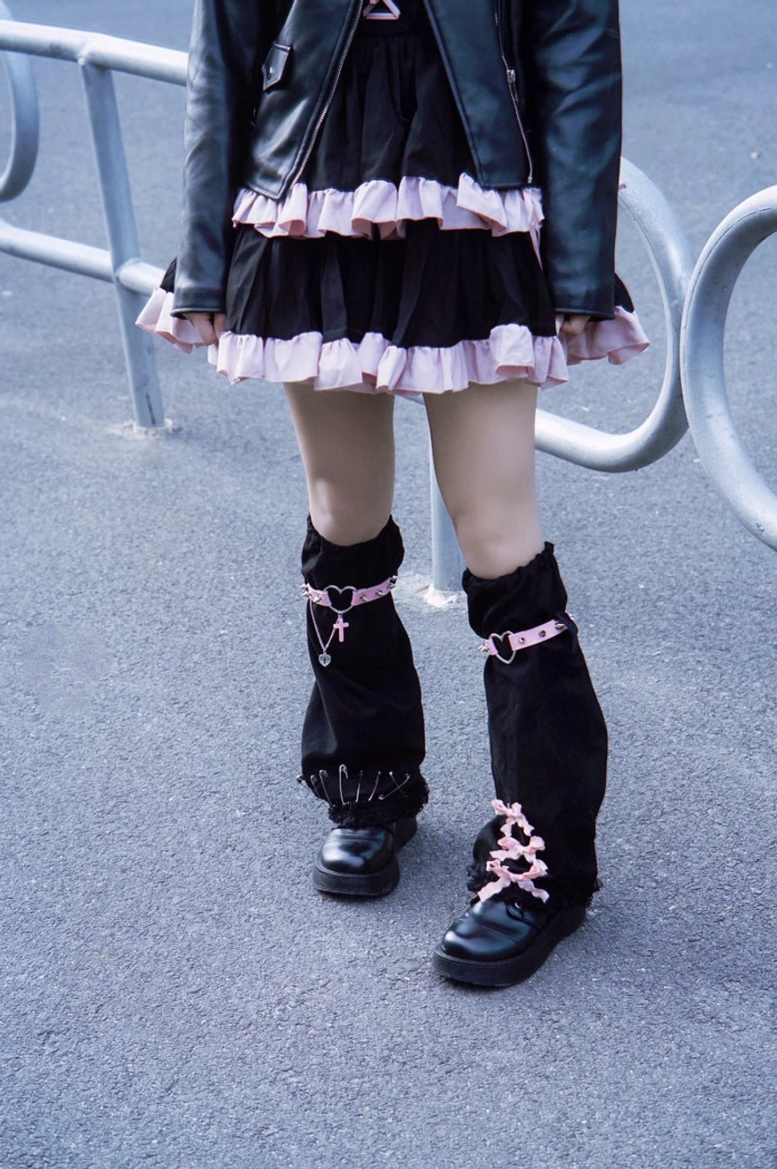 Front full leg view of gothic leg warmers with pink cross straps ribbon lace-up lower cuffs worn with leather jacket and skirt outdoor metal guardrail