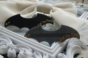 Two Gothic Lolita bat hair accessories with golden script and celestial star details arranged beside a cream bow and white frame