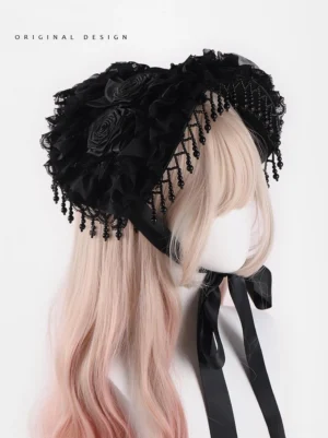 Gothic Lolita black bonnet hat with hand-knotted beaded tassel trim and handcrafted fabric roses displayed on mannequin with gradient pink-blonde curly wig, three-quarter front view showing black satin neck ties and ruffled lace base