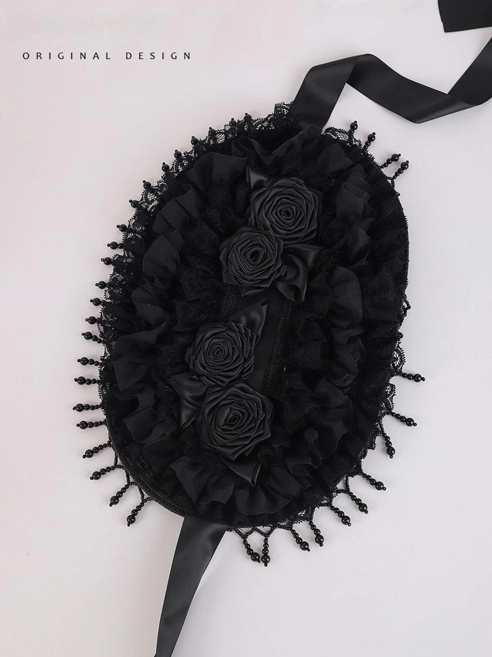 Flat lay top-down overhead view of Gothic Lolita black bonnet hat showing oval structured base, symmetrical handcrafted fabric rose ornaments, multiple ruffled layered fabric edges, and complete beaded tassel perimeter trim