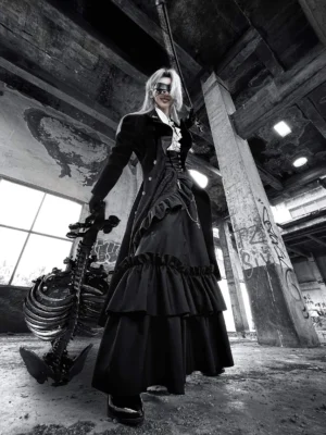 Three-quarter side angle of gothic lolita coat paired with layered black ruffle skirt and skeleton prop in abandoned industrial factory setting, displaying fitted waist construction and coat length