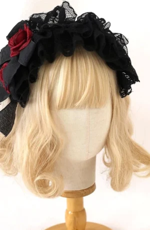 Gothic Lolita black lace KC headband with burgundy rose side decoration and black bow, worn on blonde curly wig mannequin head, front three-quarter perspective showing intricate ruffled lace layers and floral accent