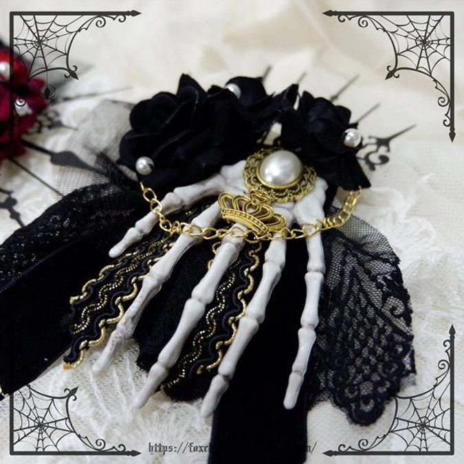 Black rose skeleton hand hair accessory close-up flat lay black fabric roses white skeleton hand gold filigree trim