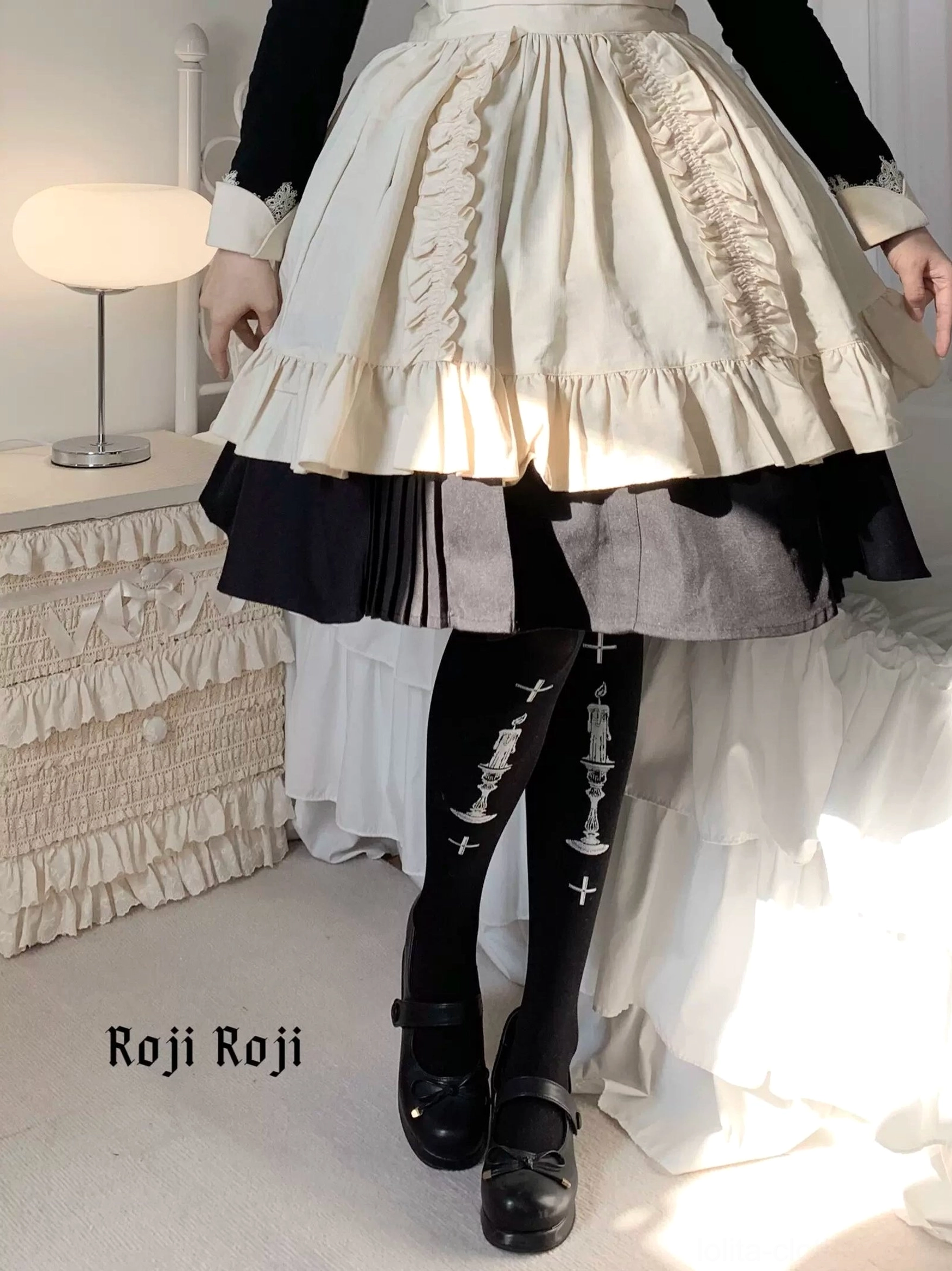 Full standing lower-body view of Gothic Lolita black velvet pantyhose with silver candle holder and cross prints paired with beige ruffled lolita skirt and Mary Jane shoes bedroom setting