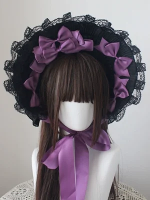 Black Gothic Lolita handmade bonnet with purple satin center bow and matching neck ribbon, displayed on mannequin with brown bangs wig, frontal flat view