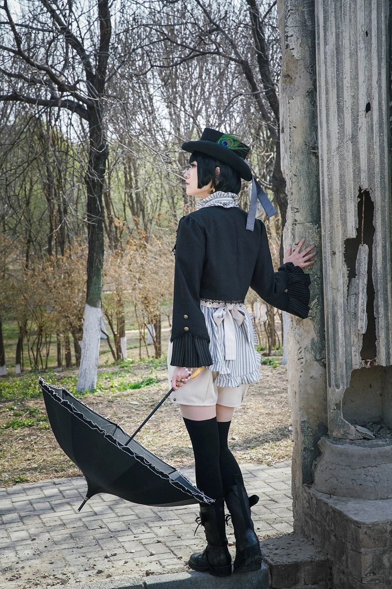Full body back distant view model wearing Gothic Lolita outfit with black cardigan jacket hand on stone pillar outdoor park scene