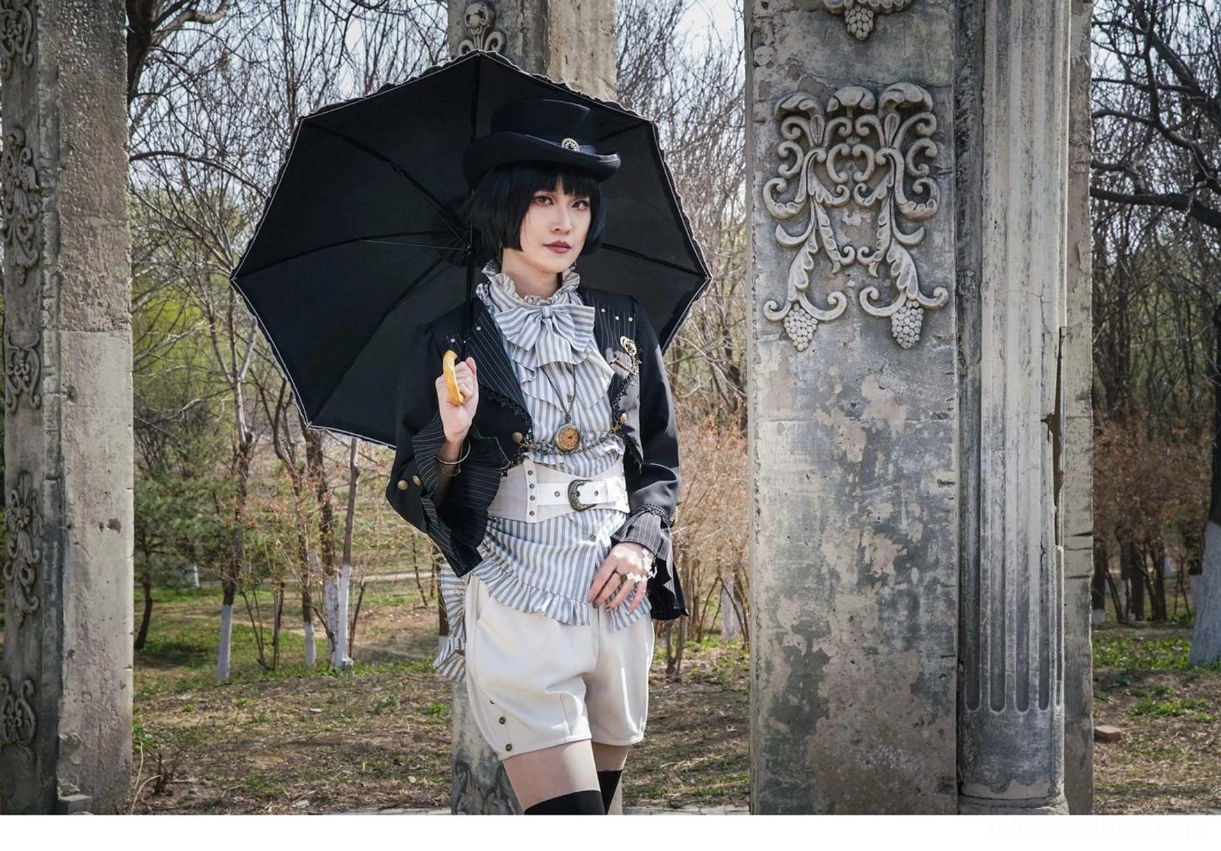 Medium full body front view model holding black umbrella by stone pillar wearing complete Gothic Lolita cardigan jacket ensemble