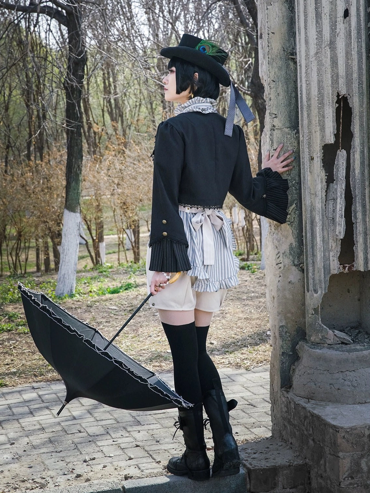 Half body side back view model in Gothic Lolita cardigan jacket posed near weathered stone pillar with black umbrella on ground