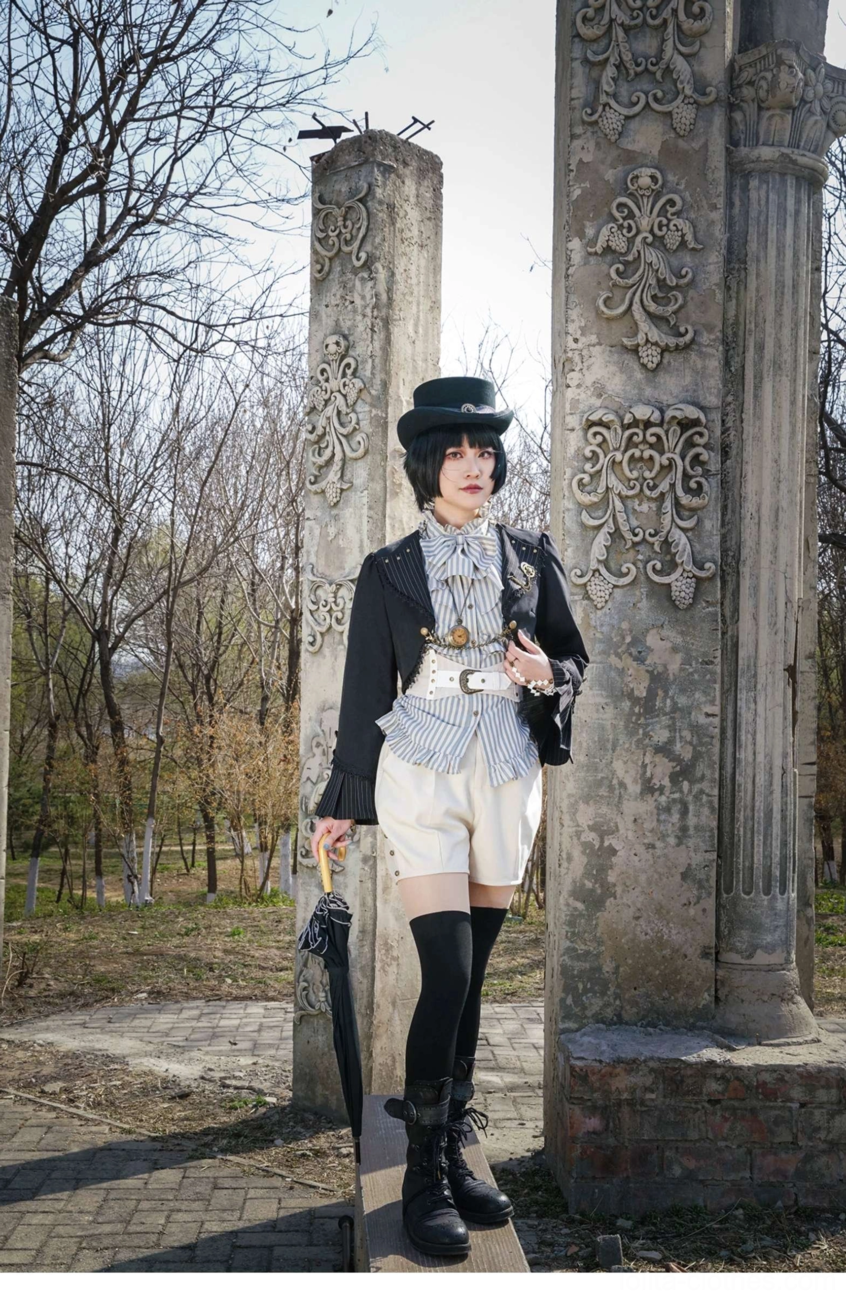 Full body side distant view model in Gothic Lolita ensemble with black cardigan jacket umbrella and outdoor vintage park setting