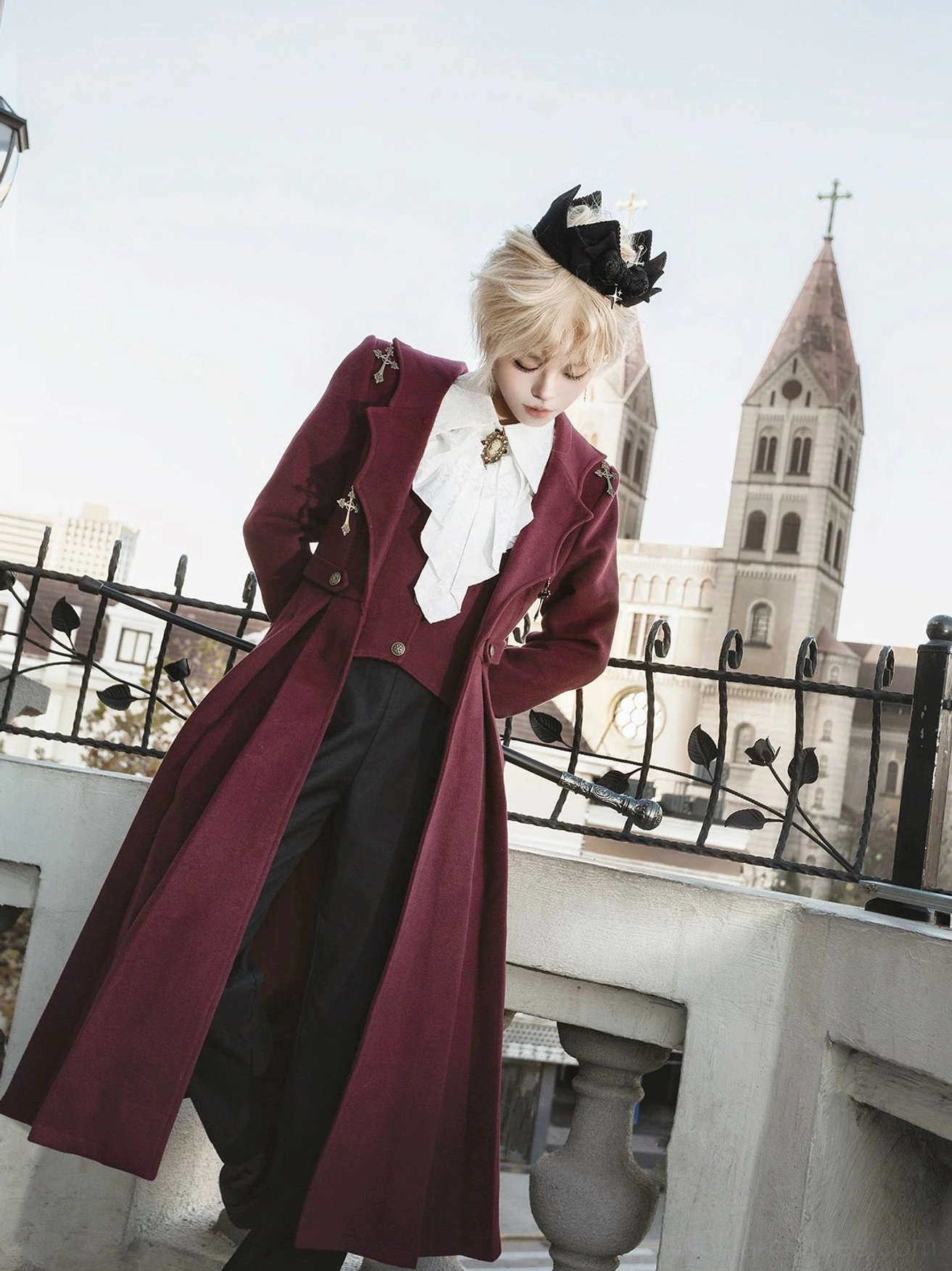 Gothic ouji lolita coat front three-quarter hands-on-hips pose open coat showing fitted waist cross brooch decoration ruffled neck cravat european balcony church spires