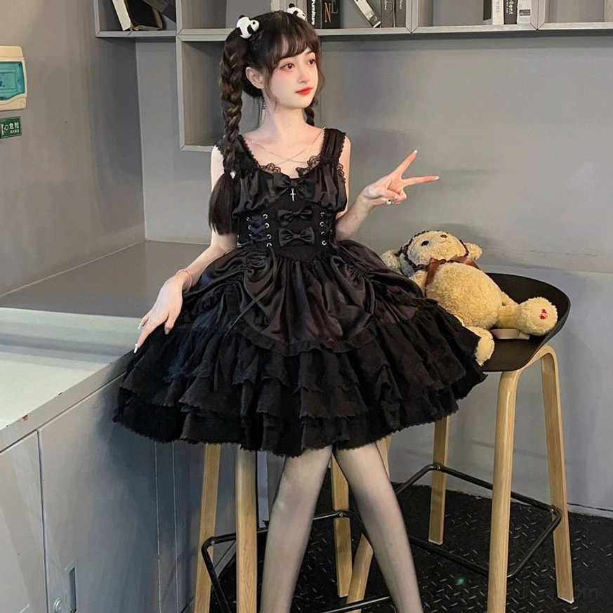 Three-quarter view of Black Cross Medal Gothic Lolita JSK dress worn with twin braids, displaying natural posing, lace-up corset waist, ruffled layered hem, and dark studio ambiance