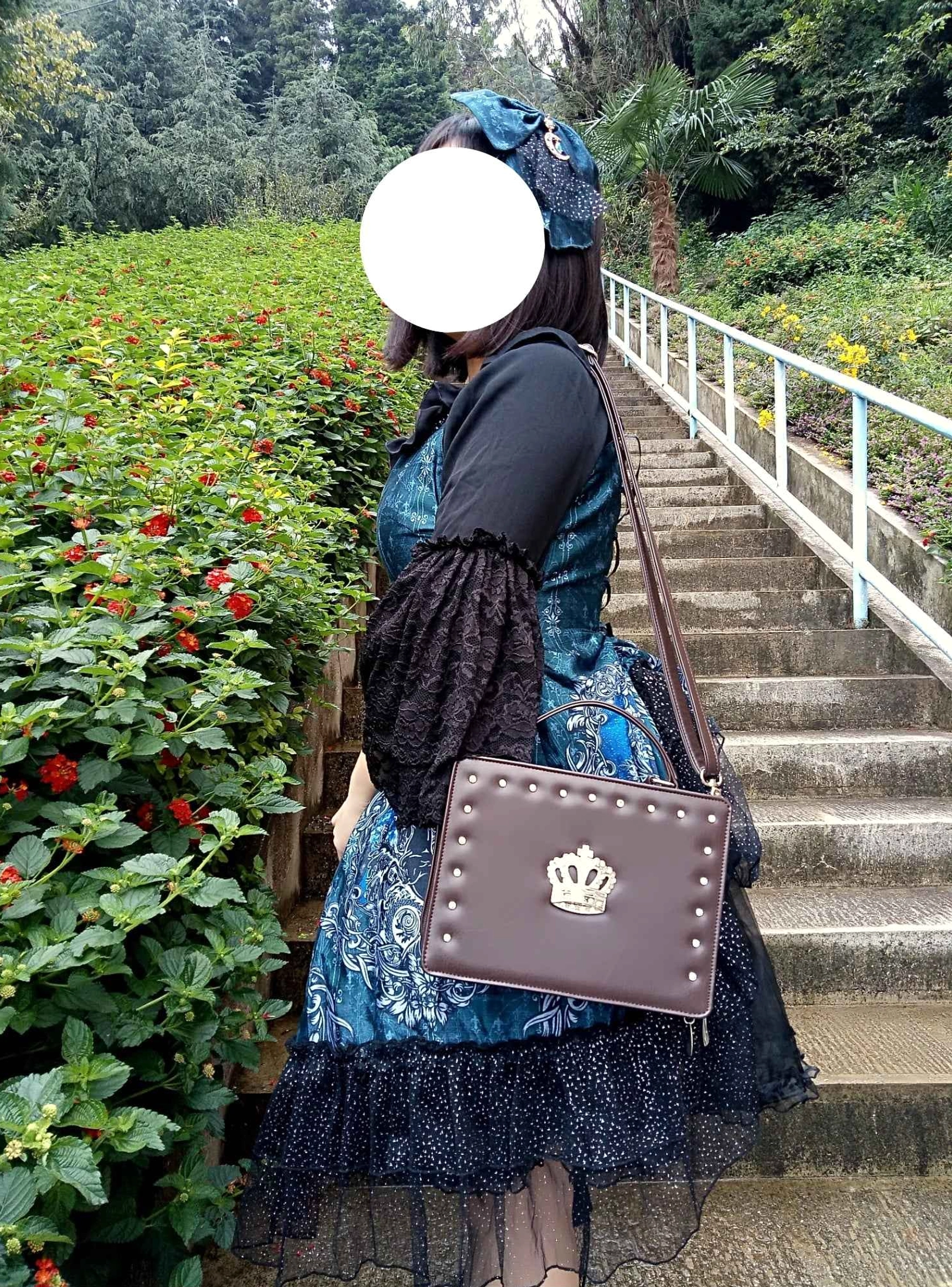 outdoor model wearing gothic lolita crossbody crown handbag side view garden stairway setting dark brown handbag central silver crown studded trim blue lolita dress