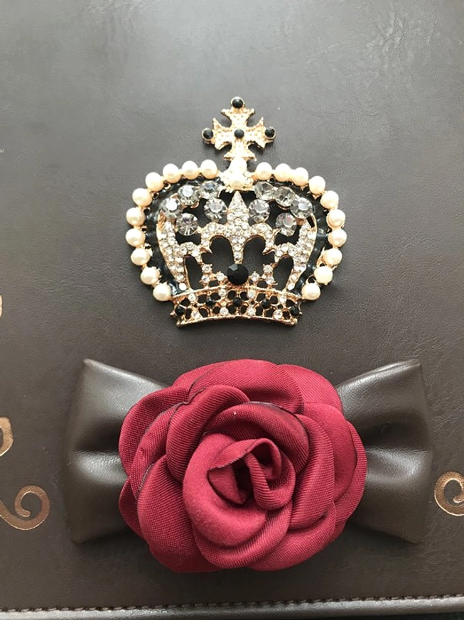 close-up detail of gothic lolita crown handbag decorative elements pearl-trimmed jeweled crown large red fabric rose black leather bow golden scroll accents dark leather