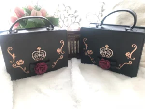 matching pair of black and dark brown gothic lolita crown handbags flat lay high angle view white fuzzy background jeweled crown red rose black bow golden scroll motifs
