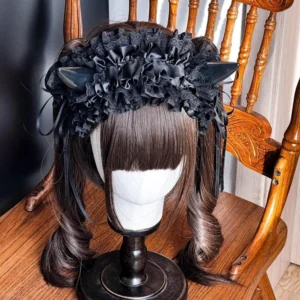 Gothic Lolita devil horn KC hairband with ruffled black lace, glossy black horns, and satin ribbon trims displayed on mannequin with twin brown ponytail wig against vintage wooden chair background