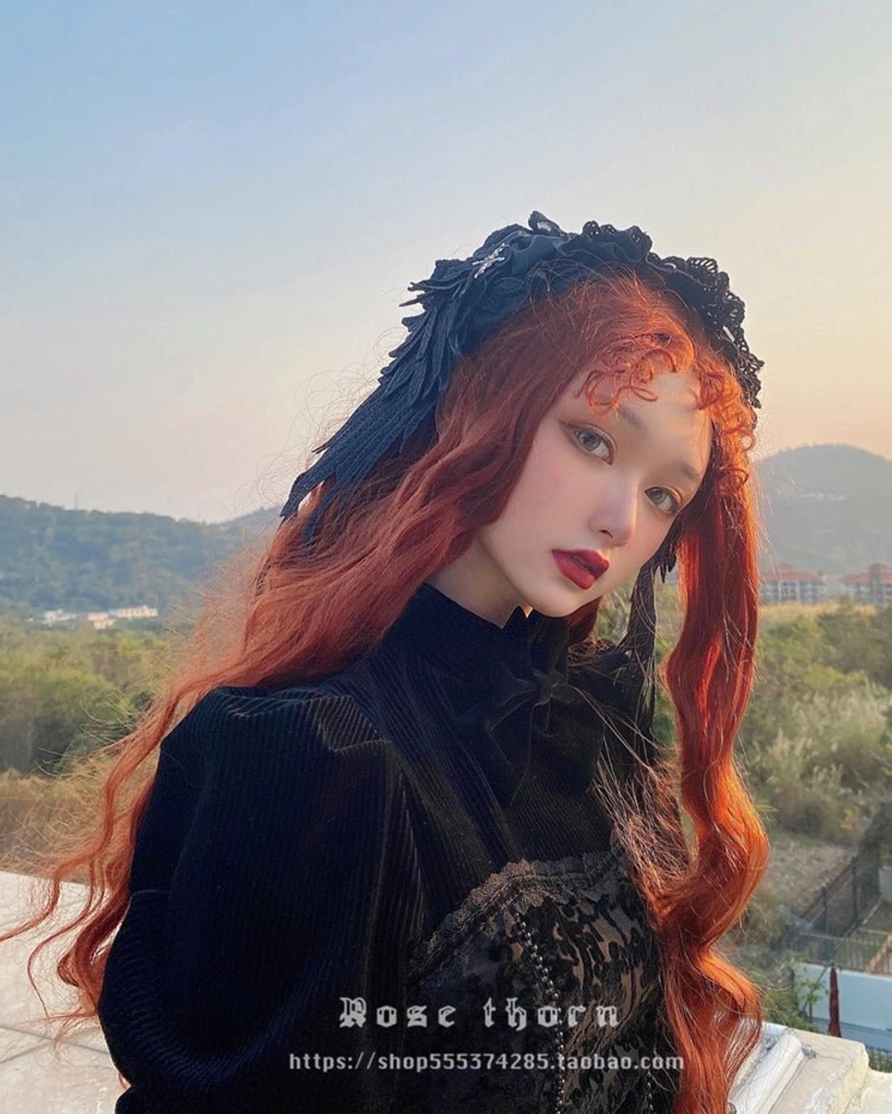 Gothic lolita headdress worn on model with long reddish curly hair in outdoor mountain setting, three-quarter front angle showing lace draping and gothic aesthetic